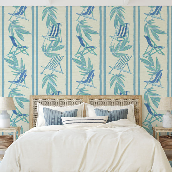 vertical linear grasscloth wallpaper print with a beachy design of blue leaves and stripes paired with shades of blue beach chairs arranged in a vertical oversized stripe Grasscloth Natural Textured Eco-Friendly Non-toxic High-quality Sustainable practices Sustainability Interior Design Wall covering bold Seaside Coastal Seashore Waterfront Vacation home styling Retreat Relaxed beach vibes Beach cottage Shoreline Oceanfront Nautical