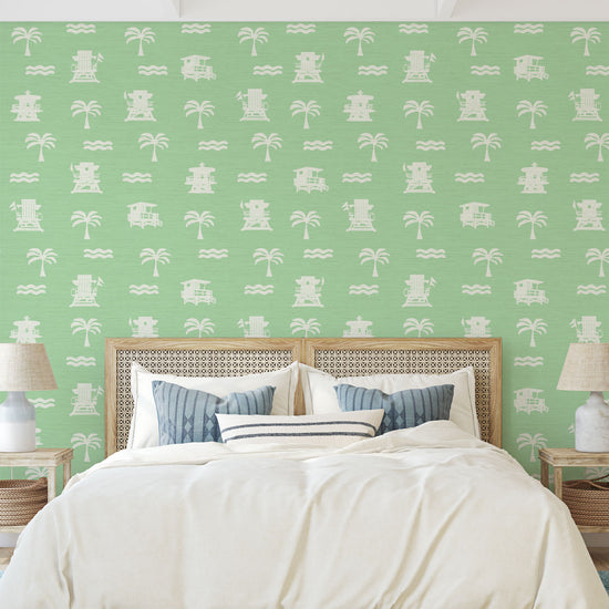 bedroom with light green (mint) base grasscloth wallpaper with white print of lifeguard stands, waves and palm trees in a mini icon print