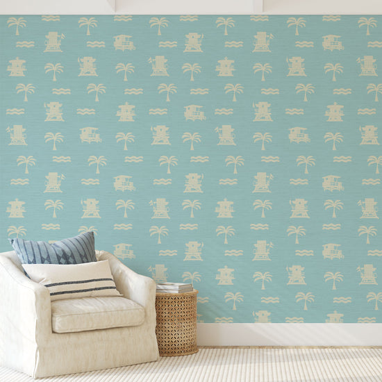 Living room with blue base grasscloth wallpaper with white print of lifeguard stands, waves and palm trees in a mini icon print
