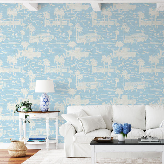 living room with grasscloth toile printed wallpaper with mid century modern houses inspired by palm springs featuring swimming pools, palm trees and secret suntanning ladies in this hand drawn one color printed design with French blue base and white print