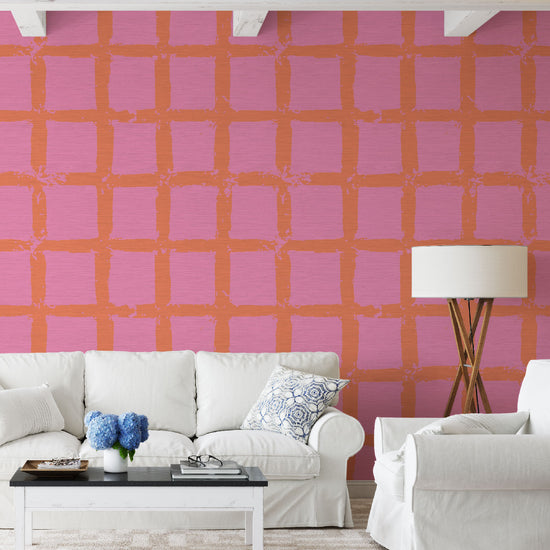 Living room with white couches in front of grasscloth wallpaper in hand painted square pattern emulating window panes in an oversized plaid layout with a pastel pink base and dark orange print